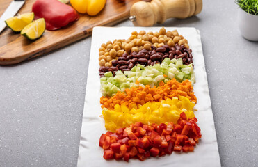 Overnight soaked chickpea, kidney beans, and chopped red, yellow bell pepper, carrot, and cucumber are stacked in a platter ready to mix in a bowl for protein salad