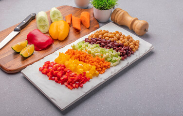 Overnight soaked chickpea, kidney beans, and chopped red, yellow bell pepper, carrot, and cucumber are stacked in a platter ready to mix in a bowl for protein salad