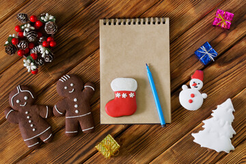 Notepad and pen, gingerbread men and gifts on a wooden table of pine boards. Preparing for Christmas and New Year's Eve, writing a holiday invitation, writing a letter to Santa and making a gift list