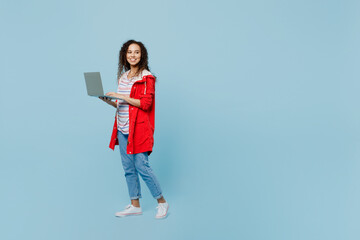 Full body young IT woman of African American ethnicity wear red jacket hold work on laptop pc...