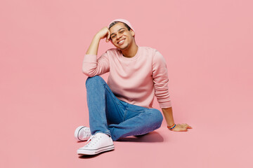 Full body happy young gay man wear sweatshirt hat sitting on floor prop up head forehead look camera isolated on plain pastel light pink color background studio portrait Lifestyle lgbtq pride concept © ViDi Studio