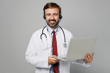 Male doctor man wears white medical gown suit set microphone headset helpline assistance use laptop pc work in call center hospital isolated on plain grey color background Healthcare medicine concept.