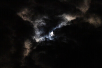 Full Moon in the night sky with dramatic clouds, dark photo with moonlight shining through