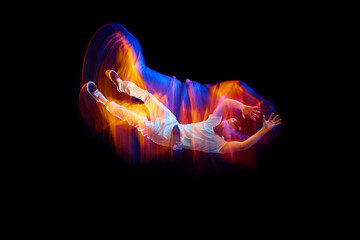 Dance in motion. Studio shot of flying, jumping dancer or gymnast performing tricks in the air over black background with mixed neon glowing rays