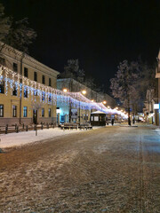 The evening street of the city in the snow is decorated with garlands for Christmas.