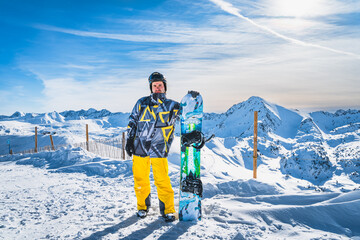Portrait of a man snowboarder with a snowboard looking at camera on the top of the snowy Pyrenees...