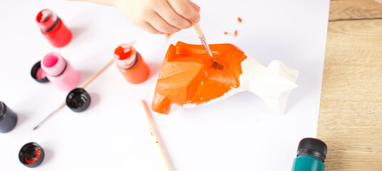 a little girl paints a toy fox made of clay. DIY concept