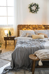 Cozy eco-style bedroom decorated for Christmas. Double bed with pillows and blankets decorated with...