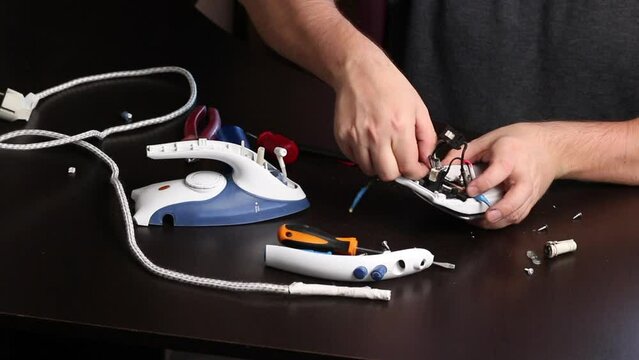 A man removes part of the burnt cord with wire cutters. Iron repair at home. Tools for repair are on the table nearby.
