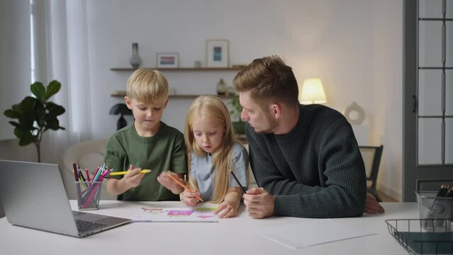 The general plan: A boy and a girl together with their dad do homework and paint a drawing with pencils. Home schooling. remote education tutoring