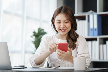 Pretty freelance asian business woman using mobile phone at working table in modern office.