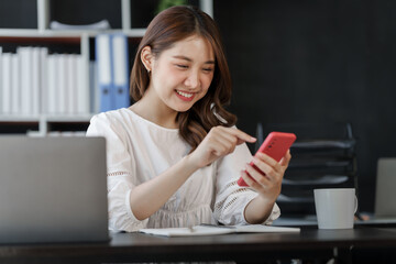 Pretty freelance asian business woman using mobile phone at working table in modern office.