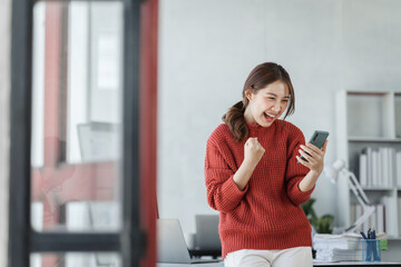 Confident Asian female office worker freelancer working in office, wearing red sweater, thai people.