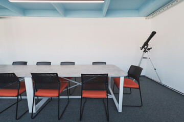 Interior of cozy light boardroom with table, modern stylish chairs and desktop computer, all ready for corporate meeting. Empty spacious office of business company or creative coworking space. 