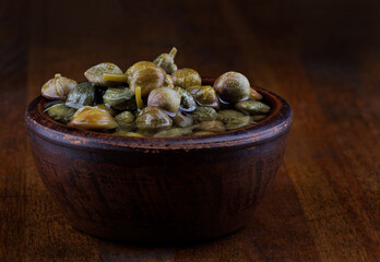 Clay bowl with capers stands on a wooden table.