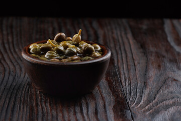 Pickled capers in a clay cup on a wooden table.