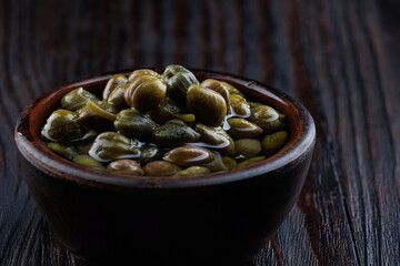 An earthenware bowl filled to the brim with capers stands on a wooden table.