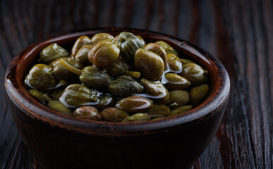 An earthenware bowl filled to the brim with capers stands on a wooden table.