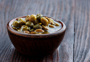 An earthenware bowl filled to the brim with capers stands on a wooden table.