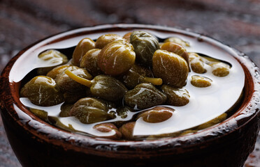 Pickled capers in brine. Clay cup full of capers.