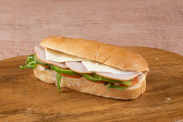 fresh submarine sandwiches with ham, cheese, bacon, tomatoes, lettuce, cucumbers and onions on dark wooden background
