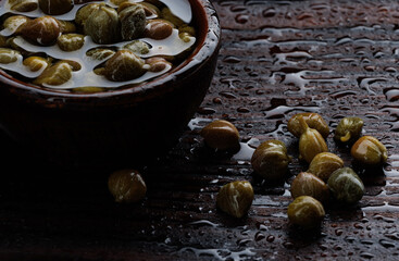 Capers in a cup and next to it on a wooden table.