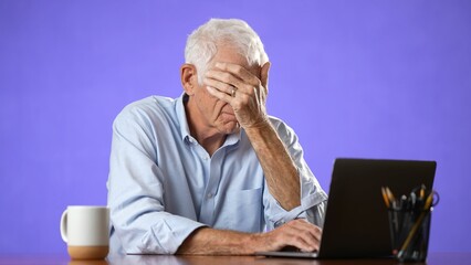 Unhappy frustrated elderly old man sitting at desk using laptop computer tired and getting bad...
