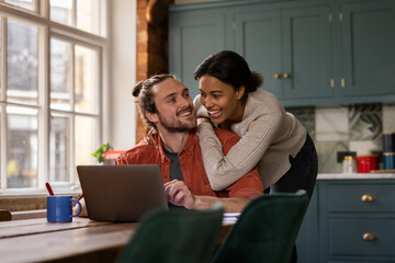Happy young adult couple at home looking at personal finances using a laptop