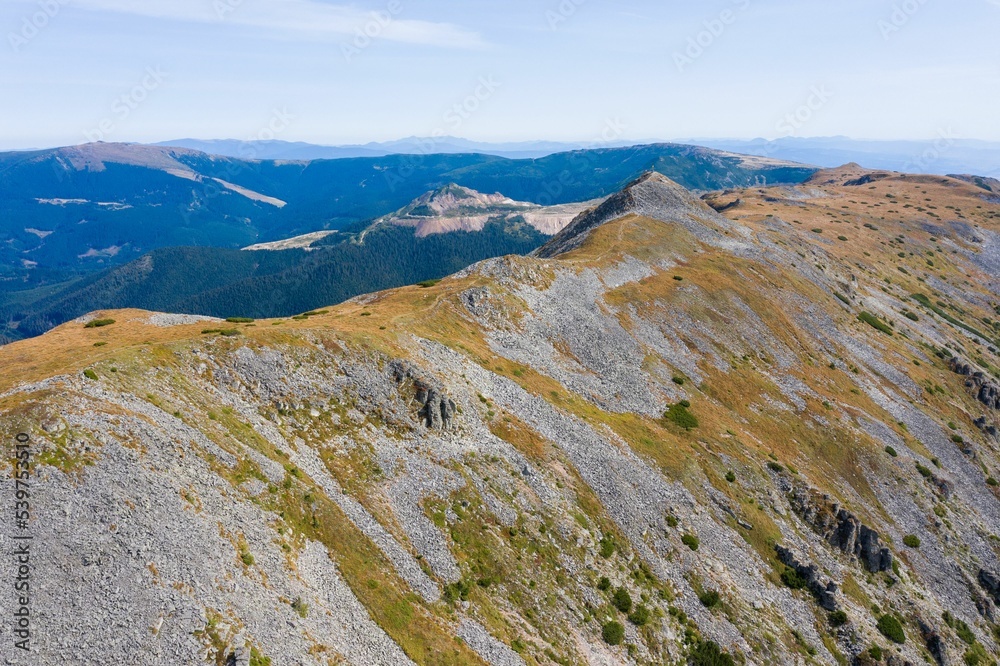 Poster view of blue cloudy sky over layered mountain ranges and valley covered with vegetation on sunny day