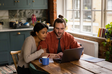 Worried young adult couple at home looking at personal finances using a laptop