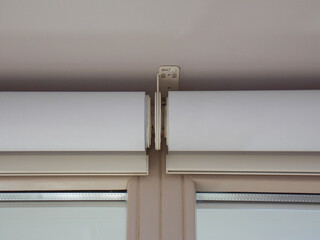 Intermediate bracket that holds two blinds together. Roller blinds close up on the window. The...