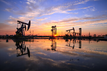 Abends laufen Ölpumpen, Die Ölpumpe und der schöne Sonnenuntergang spiegeln sich im Wasser, die Silhouette der Balkenpumpanlage am Abend.
