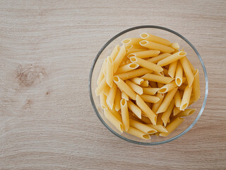 Penne-Pasta in einer Glasschale auf einem Echtholztisch bei natürlichem Licht
