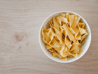 Bandnudel Pasta in einer weißen Porzelanschale auf einem Echtholztisch bei natürlichem Licht