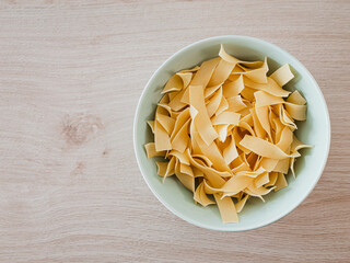 Bandnudel Pasta in einer grünen Porzelanschale auf einem Echtholztisch bei natürlichem Licht