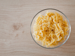 Farfalle-Pasta / Schmetterlingsnudeln  in einer Glasschale auf einem Echtholztisch bei natürlichem Licht