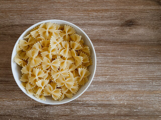 Farfalle-Pasta / Schmetterlingsnudeln  in einer weißen Porzelanschale auf einem Echtholztisch bei natürlichem Licht