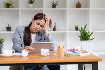 Stressed Asian businesswoman unsatisfied with her work, using portable tablet to check her email,...