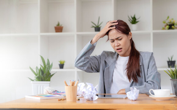 Mad Angry Stressed young asian female graphic designer or businesswoman with a crumpling paper on the table dissatisfied with her work, complained from her boss, getting a job problem.