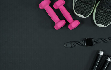 Pink dumbbell background and sports shoes smart watch skipping rope on black rubber background.fitness equipment background concept