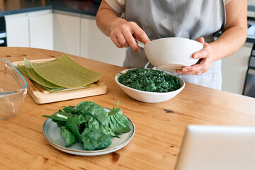Hands of woman preparing homemade spinach and ricotta lasagna. Traditional Italian dish. Selective focus.