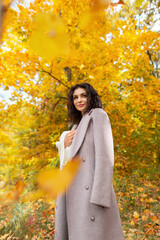 Fashionable beautiful young curly woman in a stylish autumn coat with a knitted white sweater walks in an autumn park with foliage