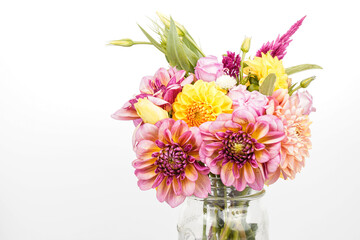 Bouquet of a variety of dahlias, celosia, and lisianthus flowers. Arrangement is placed in a glass jar. White background. Space for text.