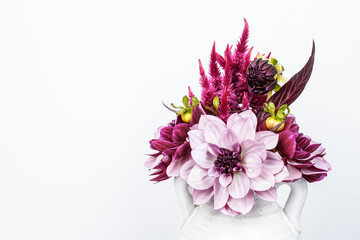 Bouquet of a variety of dahlias and celosia flowers. Arrangement is placed in a small, ceramic container with two handles. White background. Space for text. © Kathy