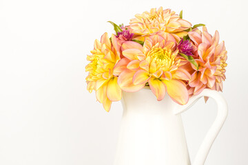 White container with handle filled with dahlia and celosia flowers. Yellow, coral, pink flowers. White background. Space for text.