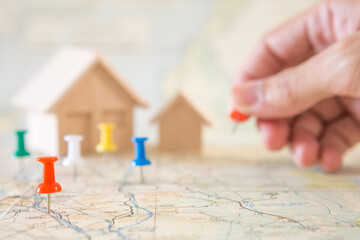 Selective focus of red pin and blurred hand holding a pin and house model on map background  for real estate concept