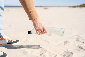 Volunteer man's hand picking up plastic bottle, collecting waste on sea beach.