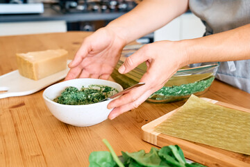 Hands of woman preparing homemade spinach and ricotta lasagna. Traditional Italian dish. Selective focus.