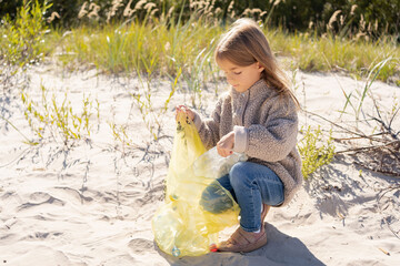little girl with trash bag cleaning up the beach. Child collects plastic, garbage on the beach by the sea.