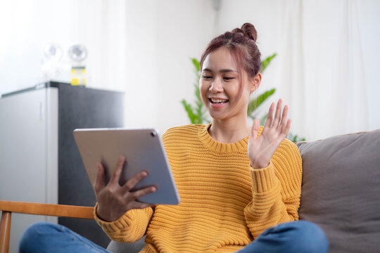Relaxed young mixed race woman in sofa smiling content, happy and reading on tablet pc at home in couch. Lifestyle image of beautiful mixed Asian girl relaxing smiling happy